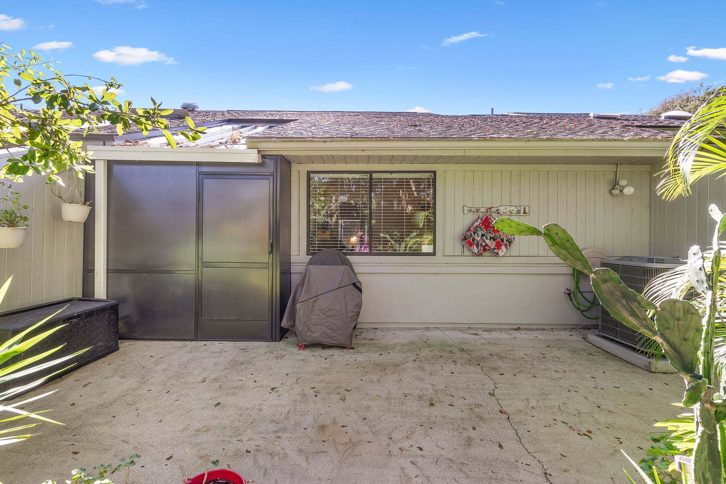 A garage with a covered grill, a window with blinds, and a cactus plant.
