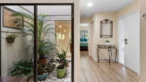 Un couloir doté d’un plancher en bois, une porte en verre donnant sur une pièce où se trouvent un lit et une petite table sur laquelle est posée une plante.