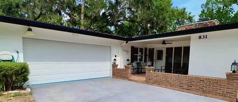 Ein Bungalow mit Garage, überdachter Terrasse und einer Ziegelmauer.
