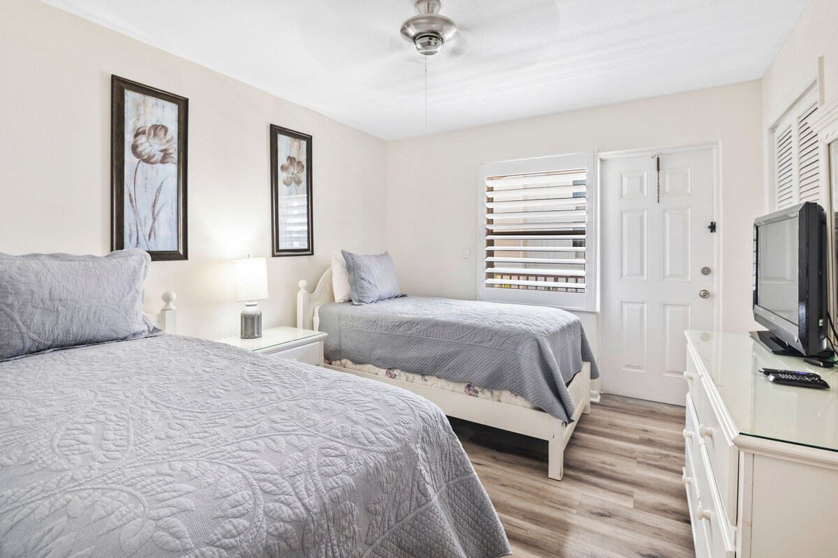 A bedroom with two beds, a television, and a door with blinds.