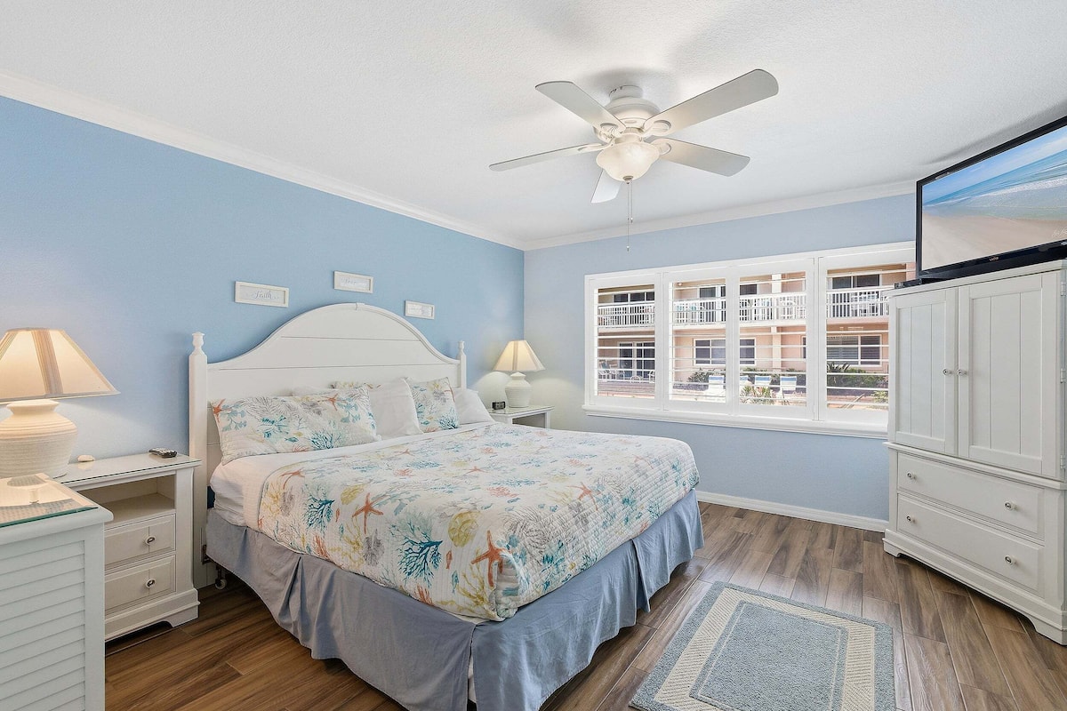 Une chambre à coucher comprenant un lit, des tables de chevet, un ventilateur de plafond, une fenêtre avec vue et une armoire.