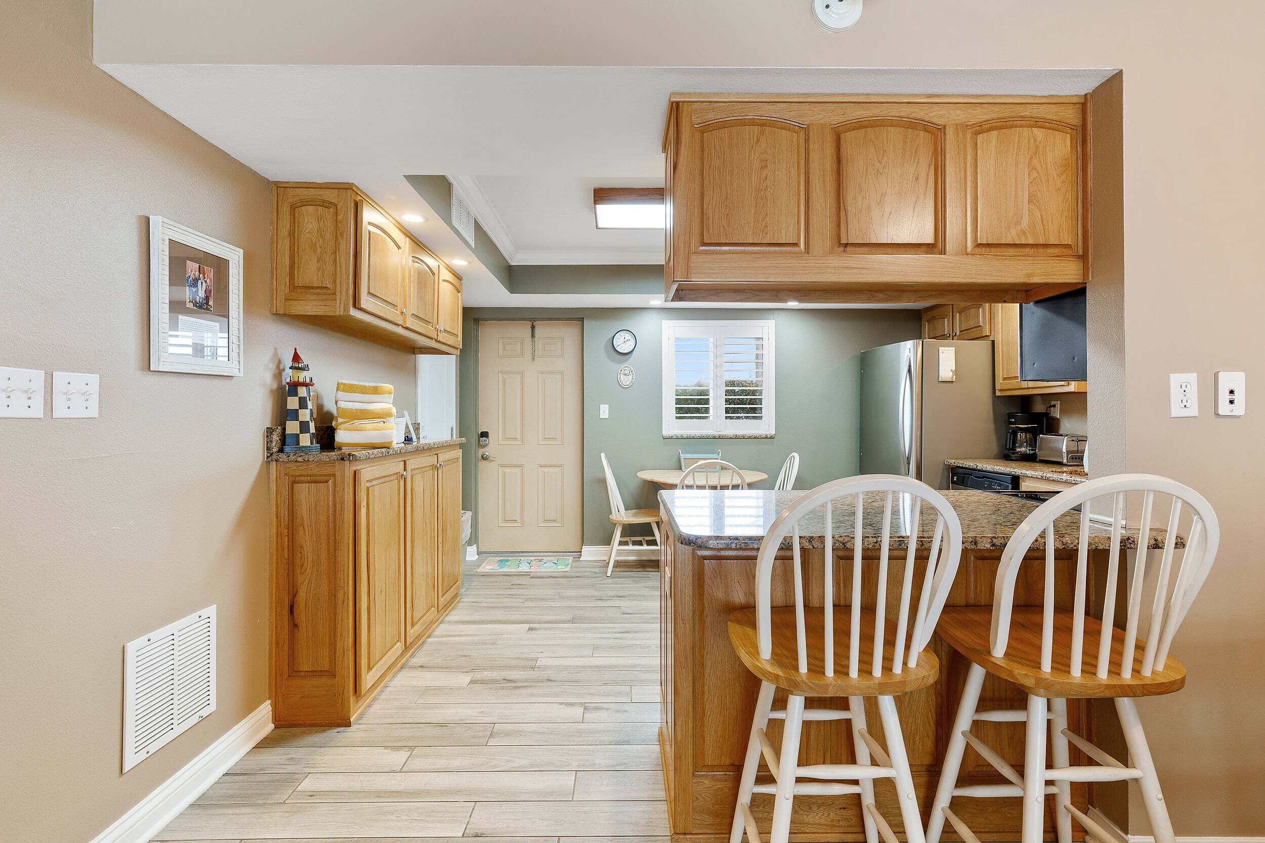 Una cocina con armarios de madera, un comedor con sillas blancas y un refrigerador.