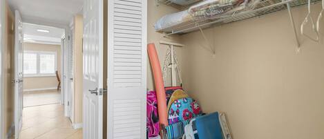 A hallway with a door, a metal shelf with folded blankets, and a rack with colorful bags.
