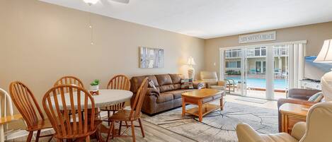 A spacious living room with a dining area, a brown leather sofa, wooden chairs, and a ceiling fan.