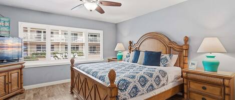 A bedroom with a bed, nightstands, a ceiling fan, a window, and a view of buildings outside.