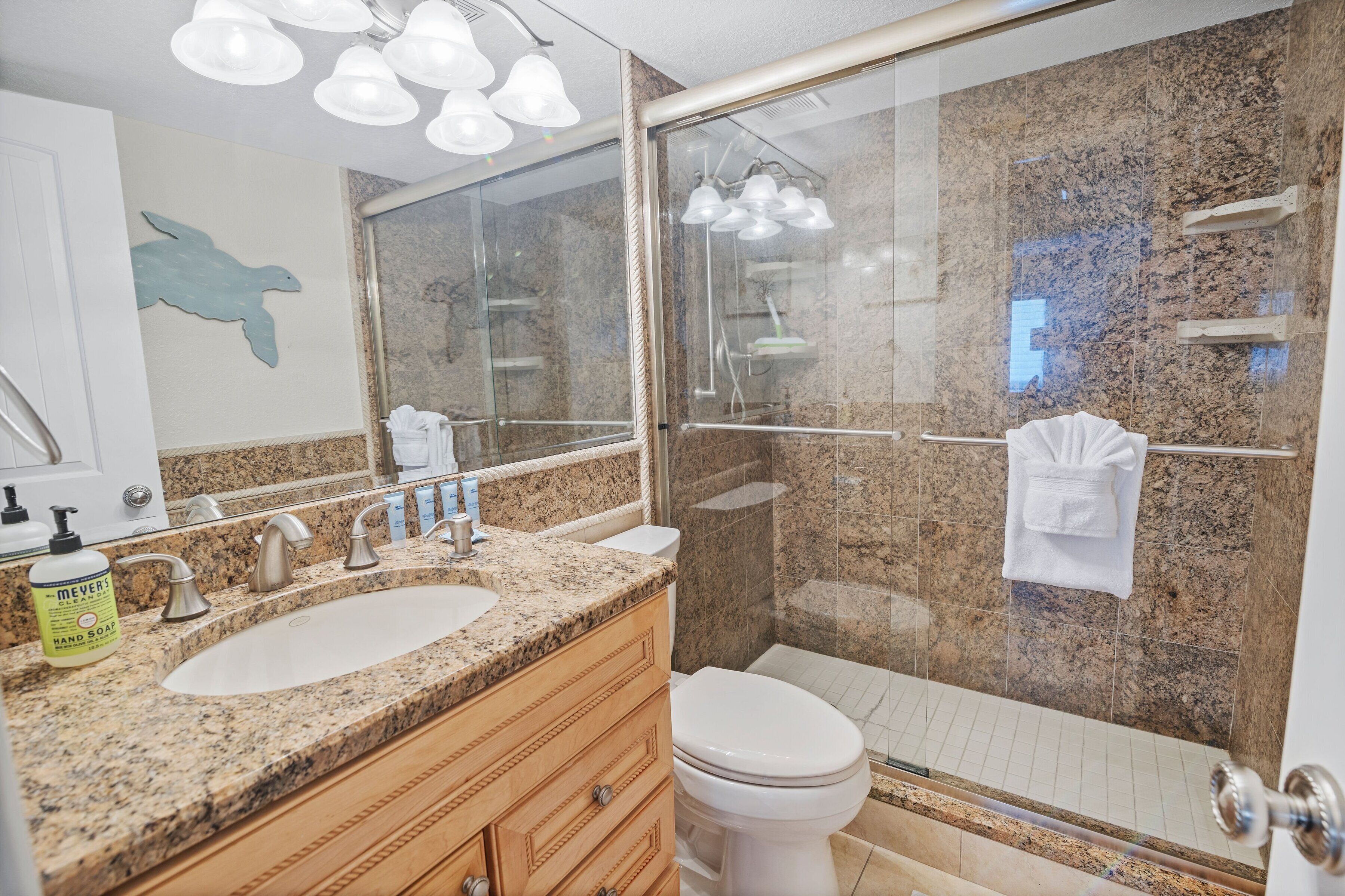 A modern bathroom with a granite countertop, double sink, and a glass-enclosed shower.