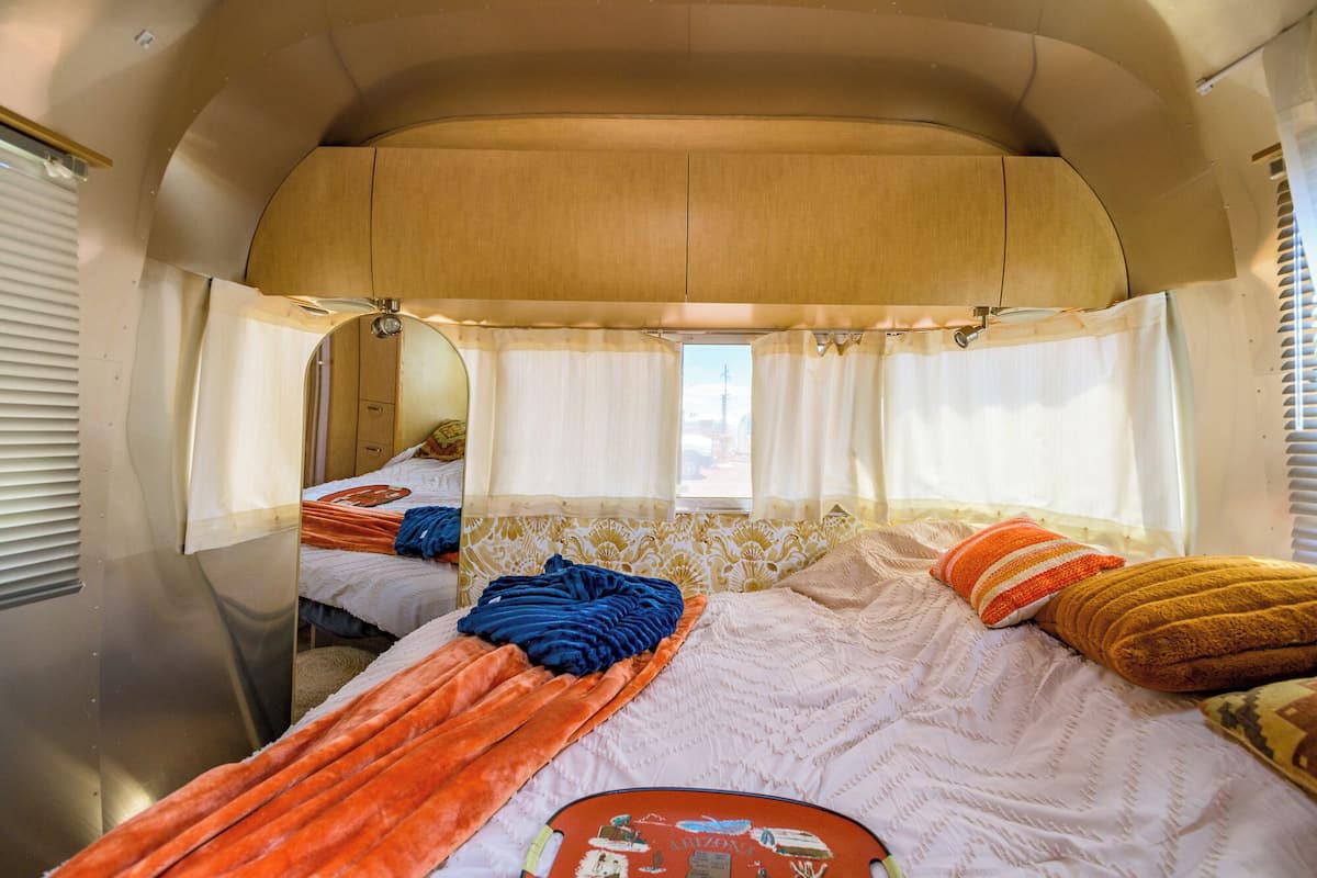Acogedor interior de una autocaravana con dos camas, una kitchenette y un ventanal.