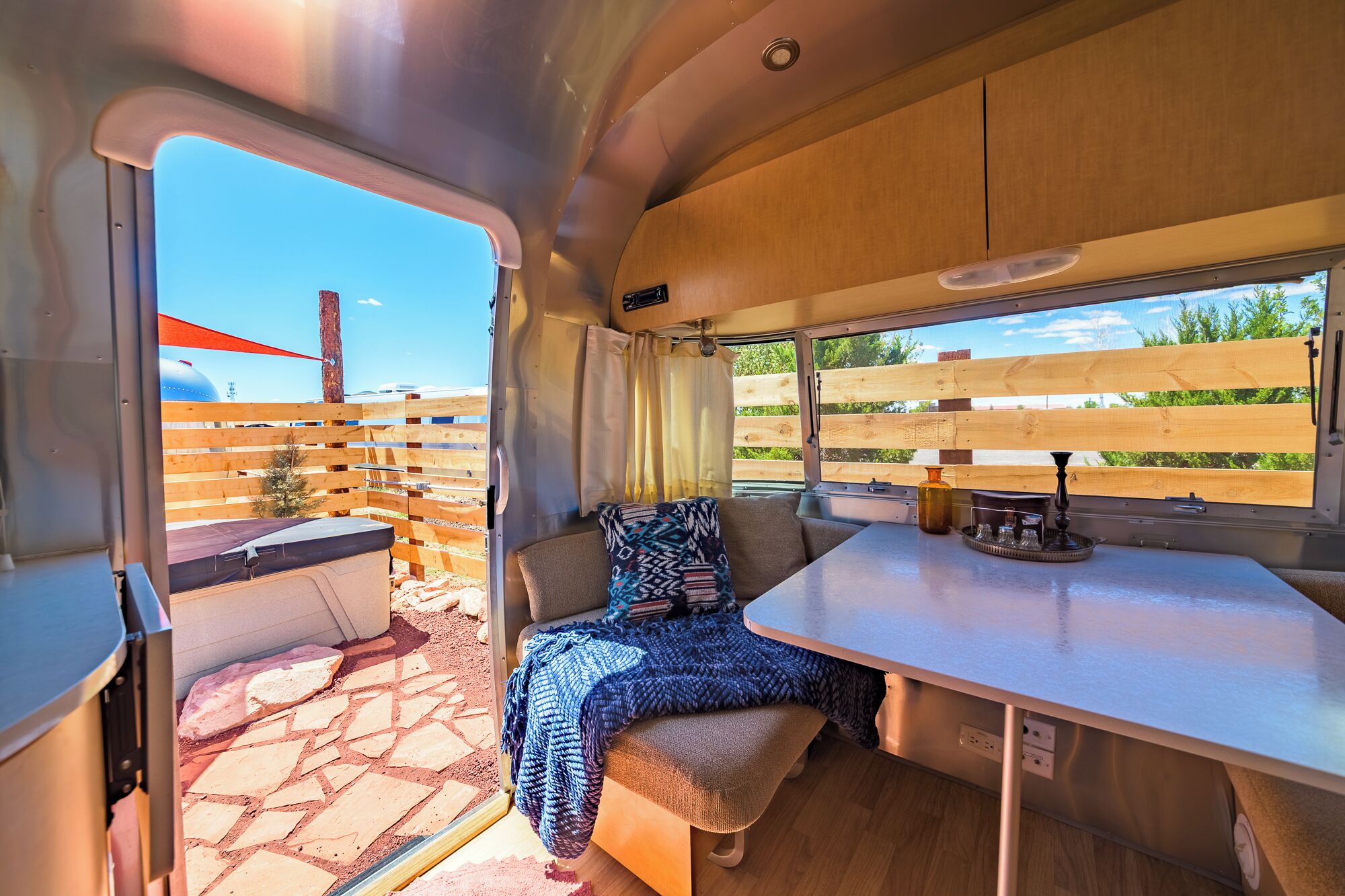 A cozy RV interior with a dining area, a cushioned seating area, and a window with a view of a fenced outdoor area.