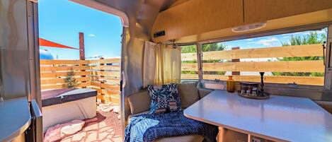 A cozy RV interior with a dining area, a cushioned seating area, and a window with a view of a fenced outdoor area.