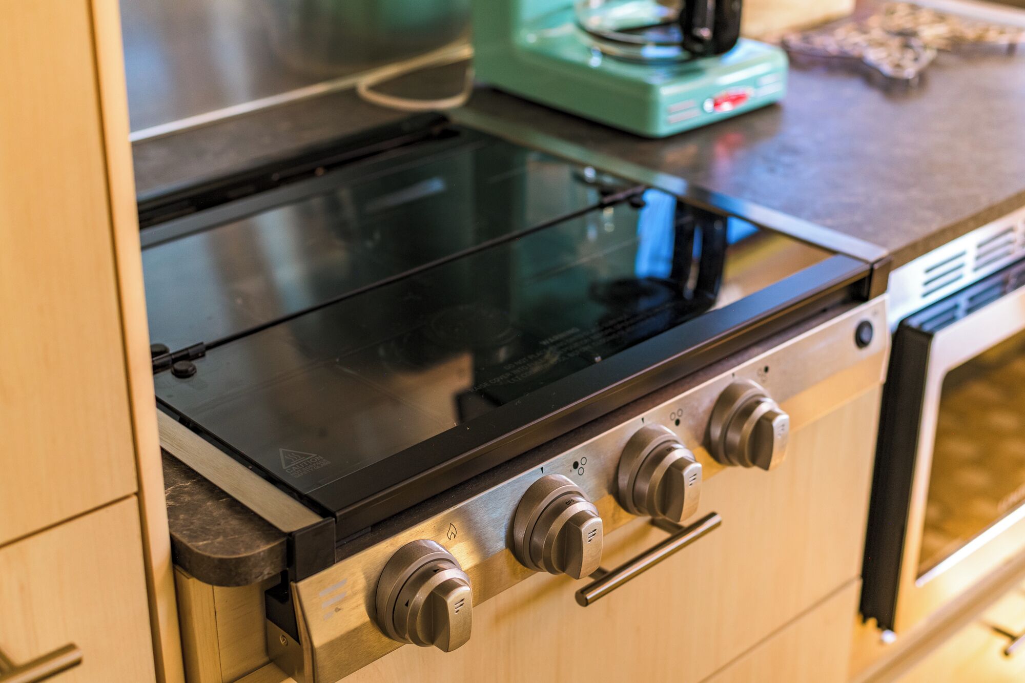 Uma cozinha com fogão preto, três botões e um eletrodoméstico verde na bancada.