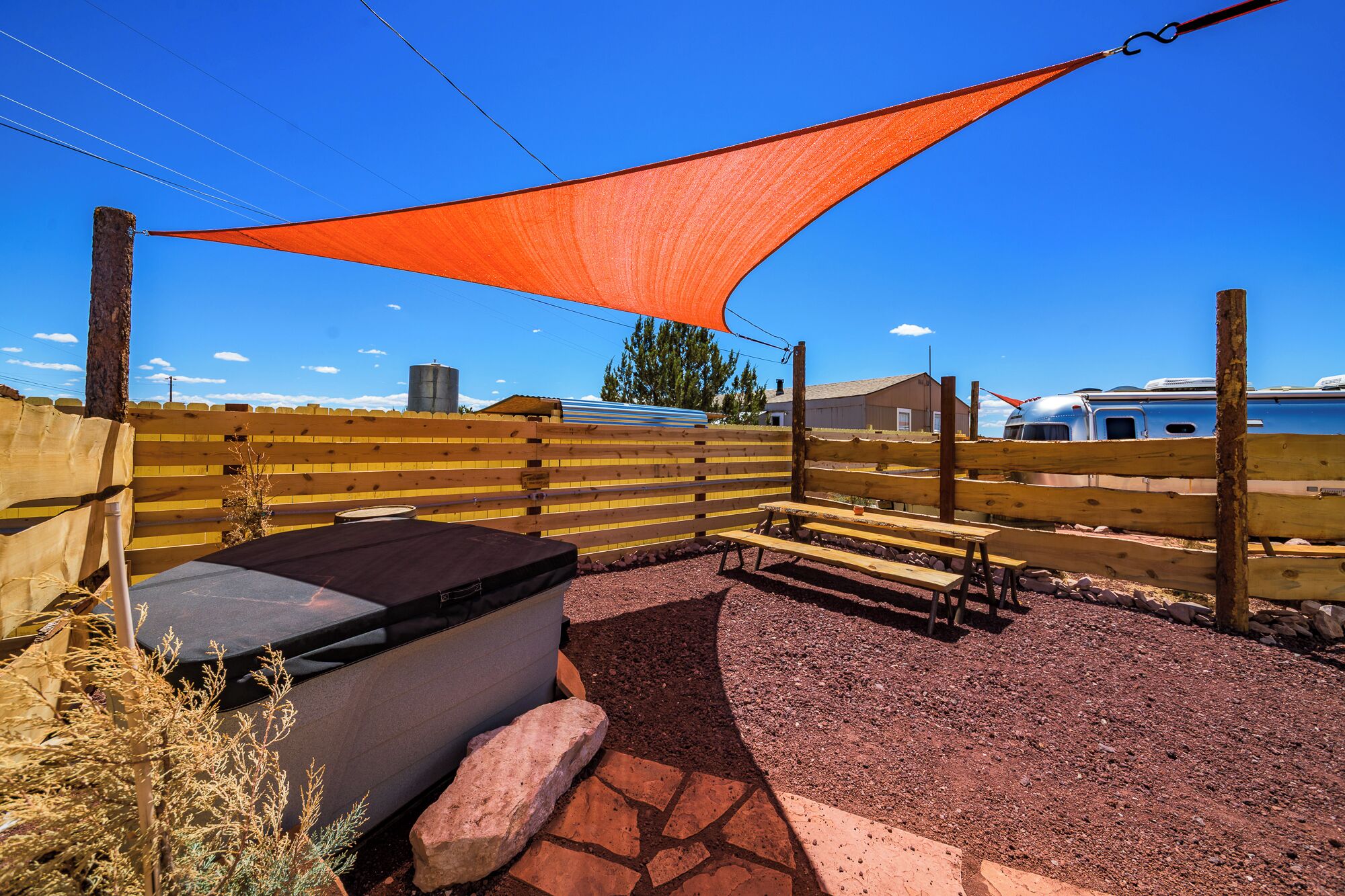 Een terras met houten omheining, een vloer van stenen tegels, een barbecue en een groot oranje zeil.