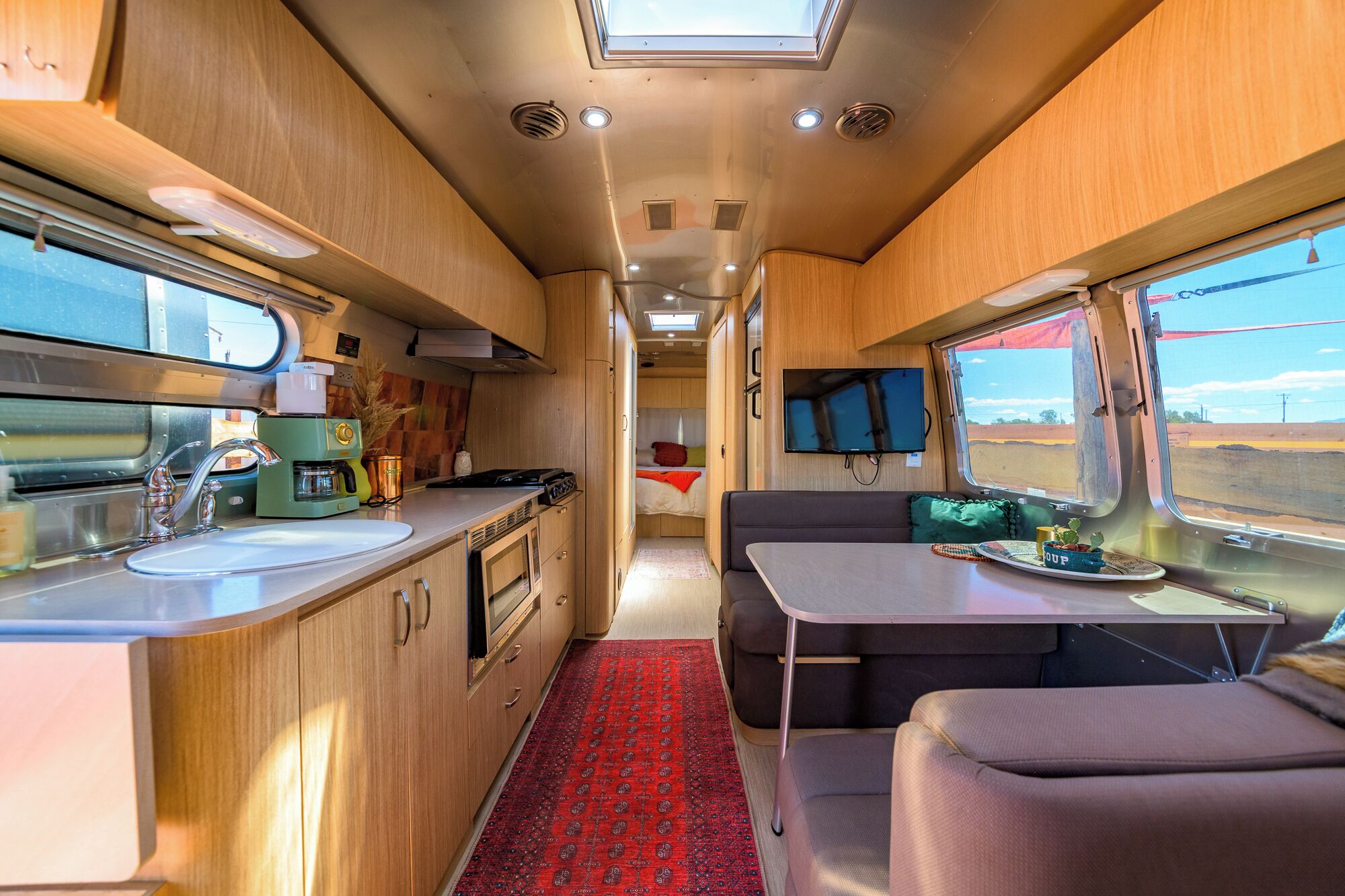 A compact RV interior with a kitchenette, a dining area, and a sleeping space.