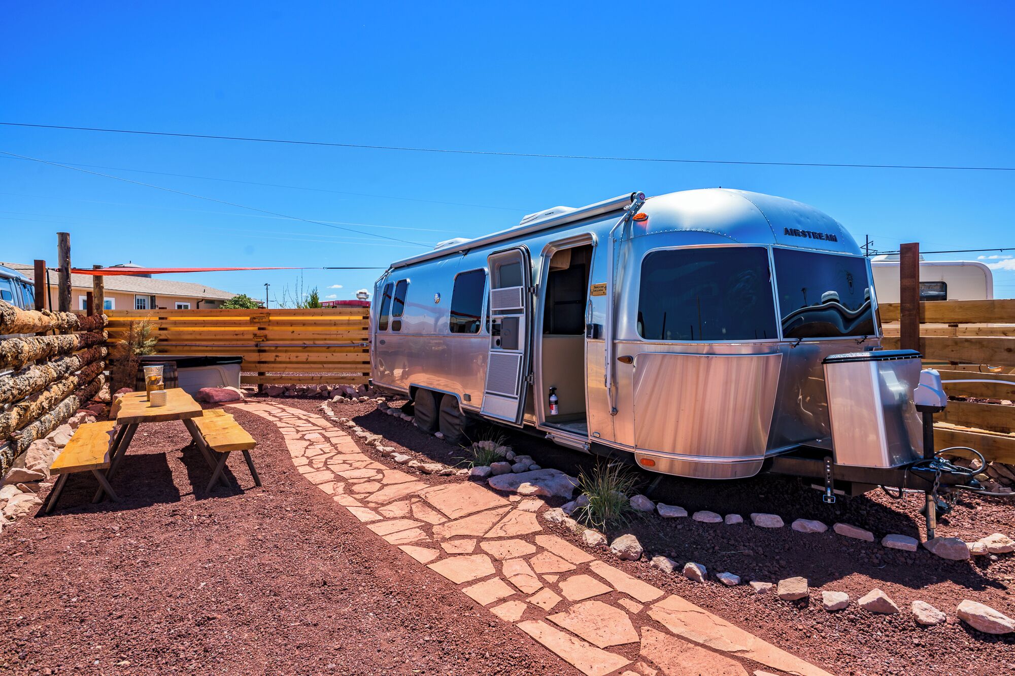 Una caravana Airstream antigua con un sendero de piedra que lleva a una mesa de picnic.