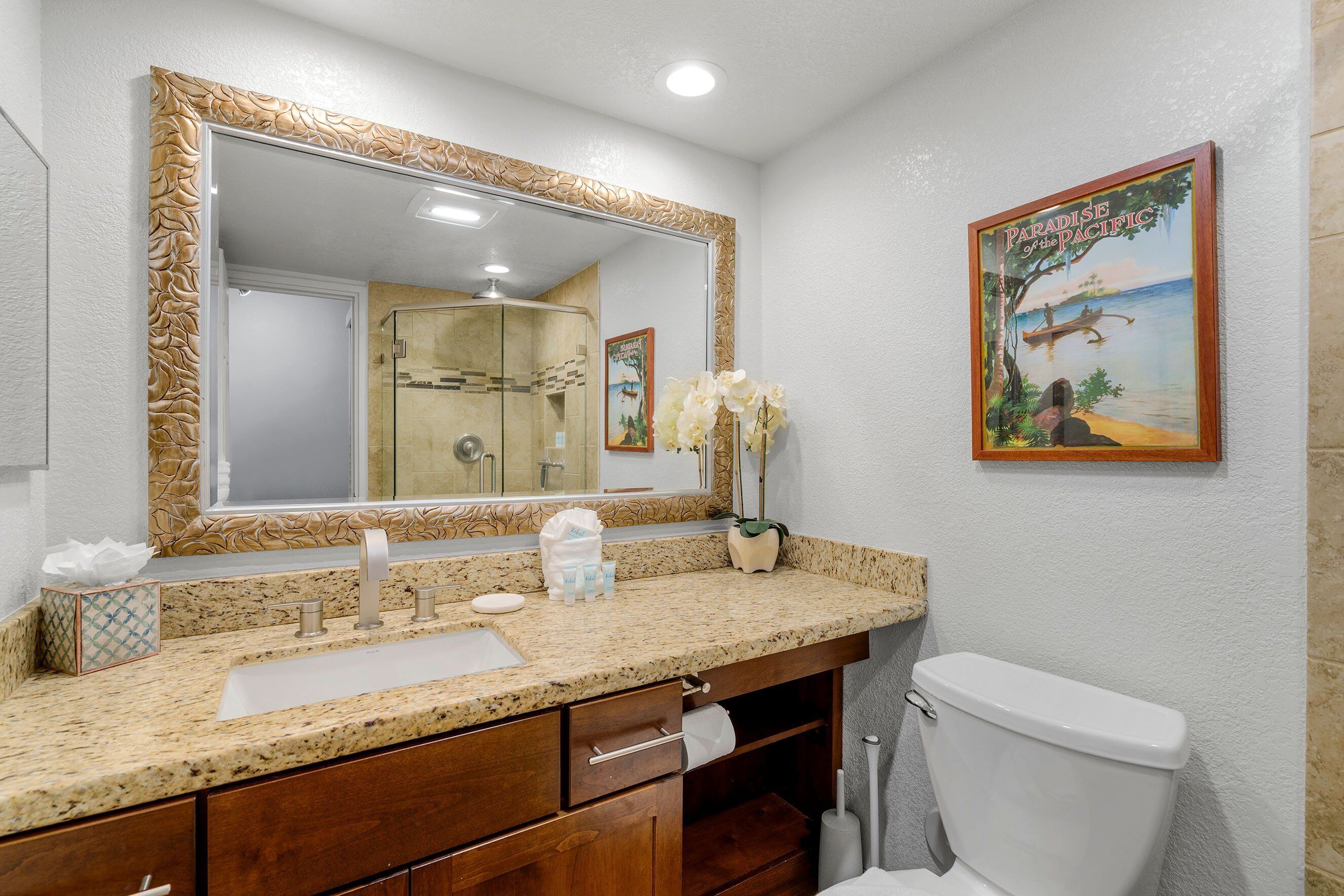 Une salle de bain avec un grand miroir, un lavabo, des toilettes et un tableau encadré au mur.