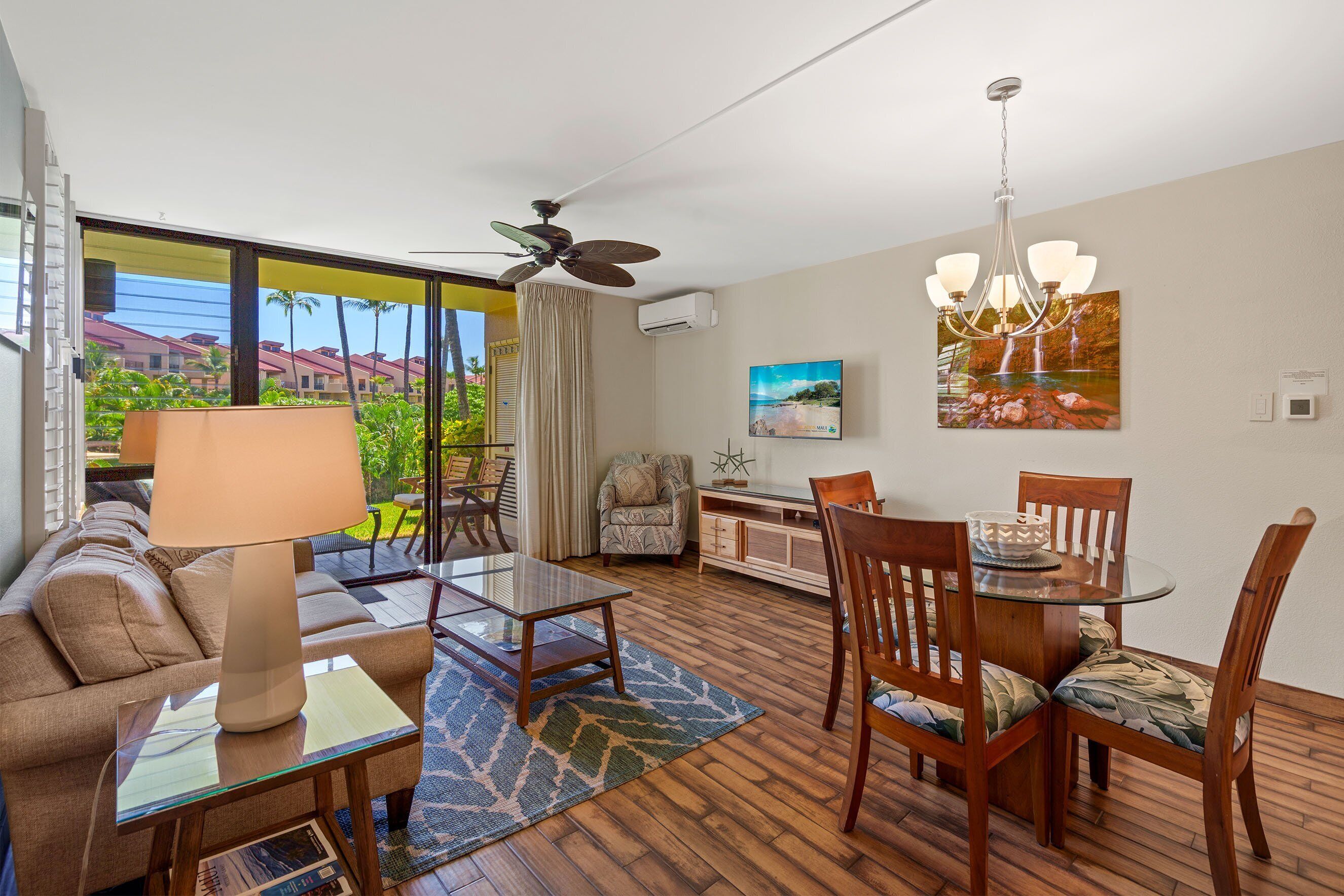 A spacious living area with a sofa, coffee table, dining table, chairs, and a ceiling fan.