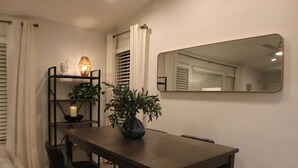 Un coin repas avec une table en bois foncé, des chaises noires, une plante en pot, une étagère avec une bougie et un miroir au mur.