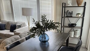 Un salon moderne avec un coin repas, comprenant un canapé, une table basse, un vase avec des plantes et une bibliothèque agrémentée d'objets décoratifs.