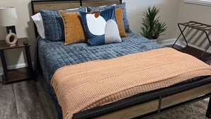 Une chambre à coucher avec un lit, une table de chevet, une lampe, une plante en pot et une fenêtre avec des stores.