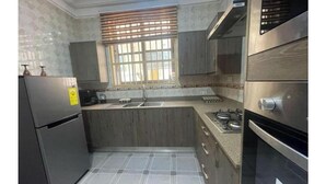 A kitchen with a refrigerator, stove, sink, and window with blinds. - KUMASI's SECRET II (Juahaw)