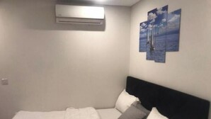 A bedroom with a bed, a headboard, a wall-mounted air conditioner, and a painting of sailboats. - KUMASI's SECRET II (Juahaw)