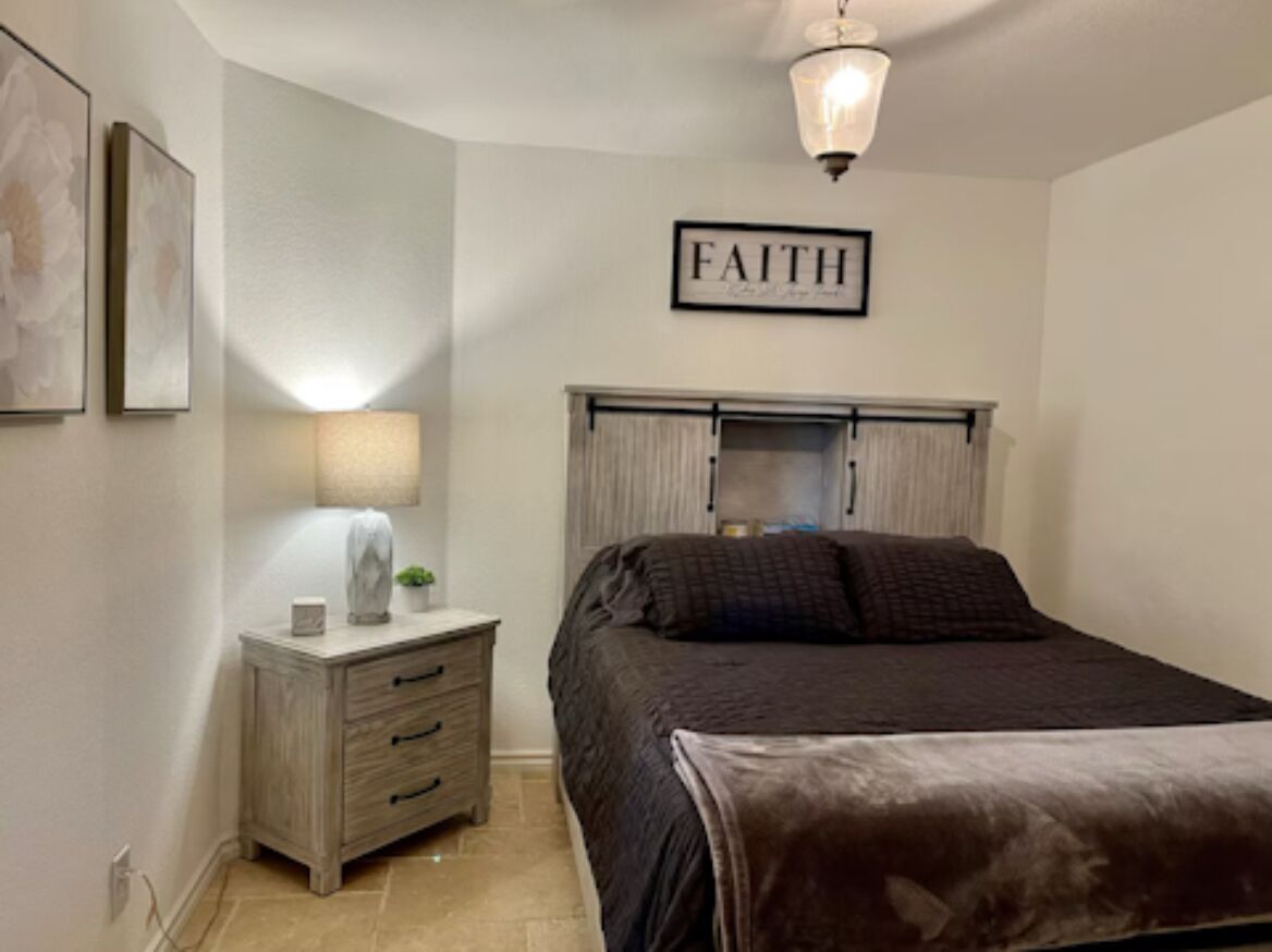 A bedroom with a bed, a nightstand, a lamp, and a wall-mounted light fixture.
