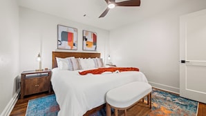 Une chambre à coucher avec un lit, un banc, un ventilateur de plafond et des œuvres d’art accrochées au mur.
