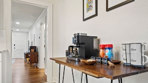 Un coin cuisine équipé d’une machine à café, de sucre, de crème et de tasses à café, le tout posé sur le comptoir.