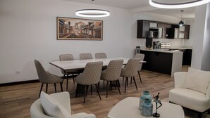 Uma sala de estar moderna com área de jantar, cozinha e uma pintura grande na parede.