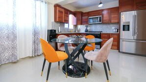 A modern kitchen with wooden cabinets, a stainless steel refrigerator, a microwave, and a gas stove. There is a glass dining table with four chairs. - Edificio Amber (San Cristobal)