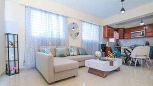 A living room with a sofa, coffee table, and a dining area with chairs and a kitchen in the background. - Edificio Amber (San Cristobal)