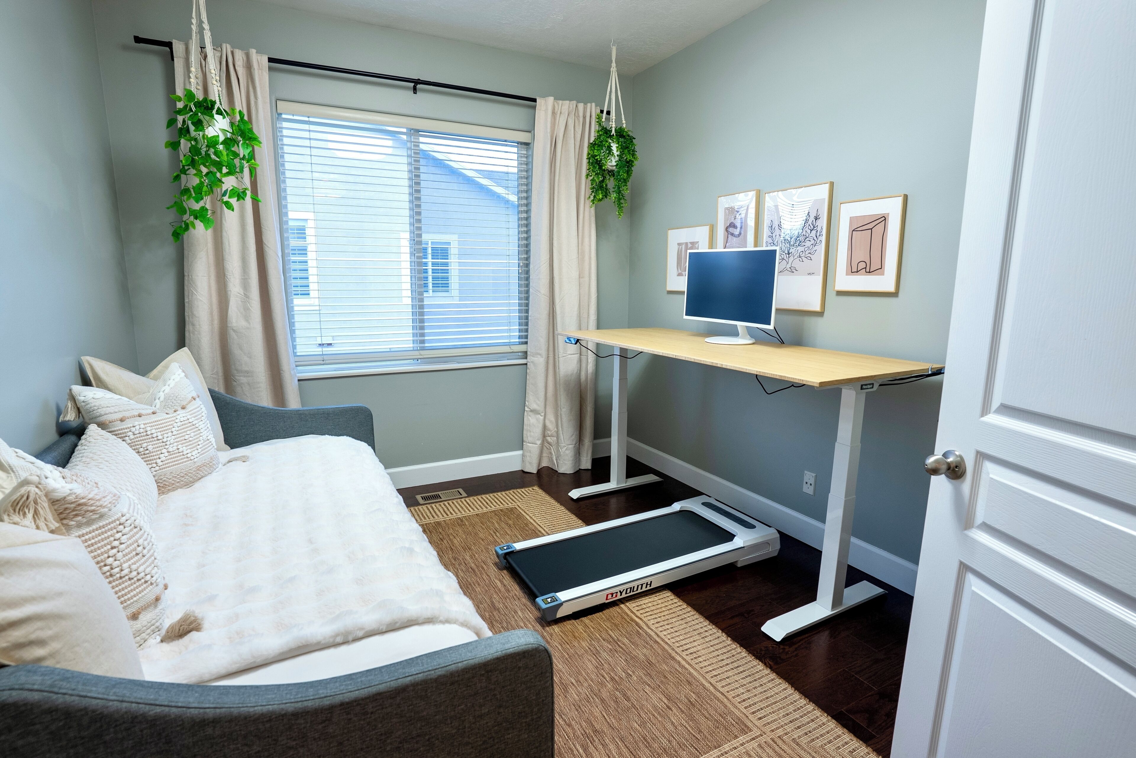 Un dormitorio con cama, cinta de correr, escritorio con computadora y ventana con cortinas.