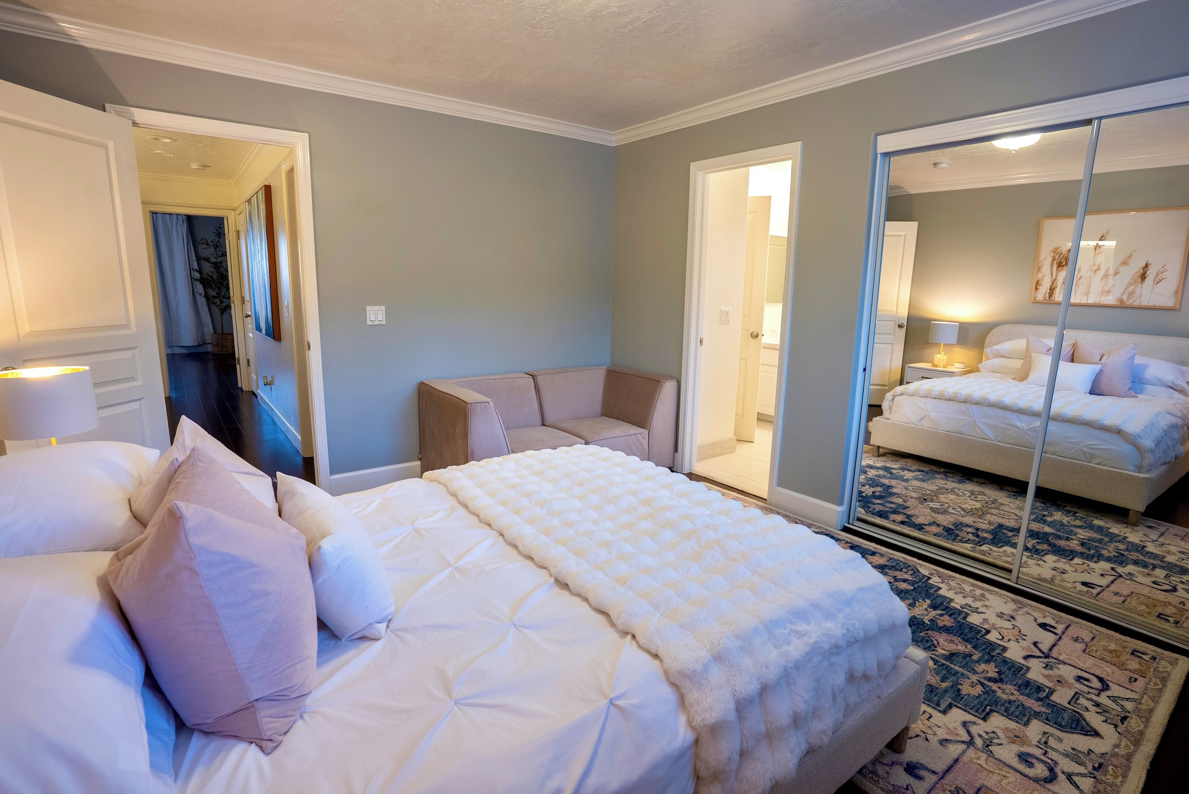 A hotel room with a large bed, a sitting area with a sofa, and a mirrored closet.