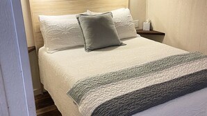 Una cama bien hecha con una colcha blanca texturizada y una manta gris.