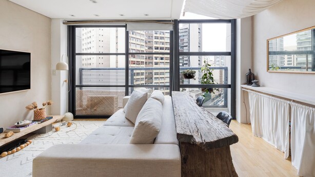 A modern living room with a large window, a sofa, a wooden table, and a TV mounted on the wall. - Urbano Duplex by WECARE Hosting (São Paulo)