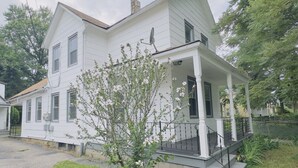 A two-story white house with a porch and a small garden with blooming flowers. - Zen Den Getaway, your peaceful retreat near Cleveland’s vibrant AsiaTown. (Cleveland)