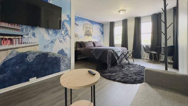 A modern hotel room with a bed, a TV mounted on the wall, a small round table, and a seating area with a chair. - Zen Den Getaway, your peaceful retreat near Cleveland’s vibrant AsiaTown. (Cleveland)