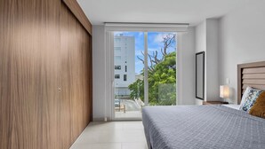 Une chambre moderne avec un grand lit, une armoire en bois et une porte-fenêtre coulissante donnant sur un balcon avec vue sur la ville.