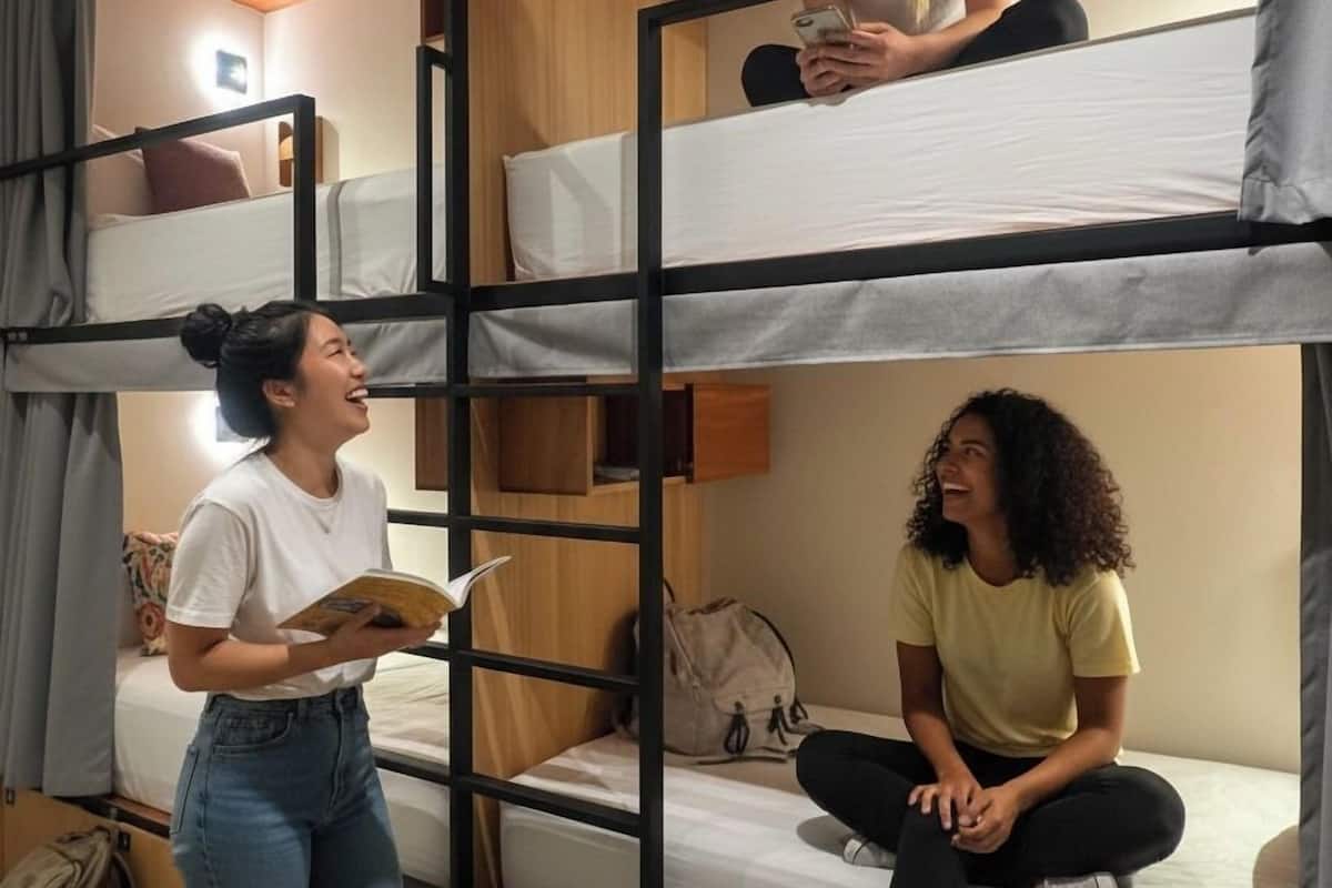 A bunk bed room with a wooden bunk bed, a single bed, and a suitcase on the floor.