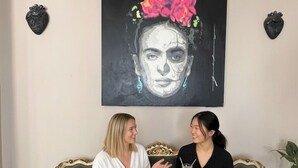 Dos personas sentadas en un sofá antiguo con un cuadro abstracto grande sobre ellas.