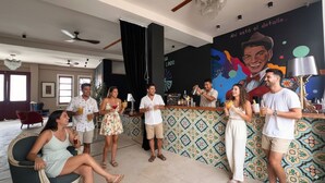 Un grupo de personas en una zona de bar con una pared decorada y un cartel grande al fondo.