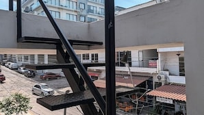 Una terraza al aire libre de varios niveles con una escalera de metal, vista a un edificio con balcones y un pequeño espacio de estar exterior.