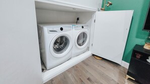 A compact laundry room with two front-loading washing machines, a white cabinet, and a green wall.