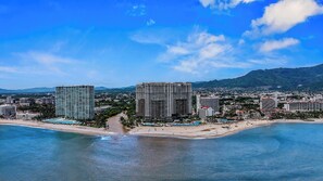 Un paysage urbain côtier avec de grands hôtels, une plage et des montagnes en arrière-plan.