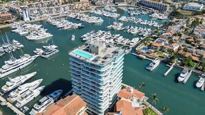 A marina with numerous yachts docked, a high-rise building with balconies overlooking the water, and a residential area with palm trees. - Marina Vallarta with View and Pool (Puerto Vallarta)