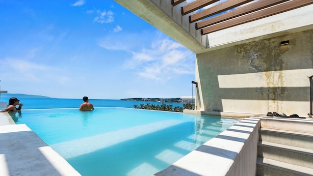 A clear blue infinity pool with a view of the ocean, steps leading into the pool, and a person swimming. - One block from the beach in Bucerias (Bucerías)
