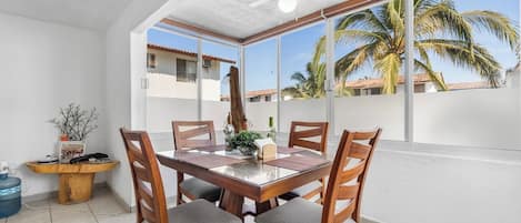 A dining area with a table and chairs, a ceiling fan, and a view of palm trees through large windows.