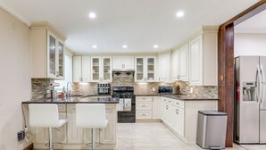 Une cuisine moderne avec des meubles blancs, un îlot central doté de tabourets, des appareils en acier inoxydable et un dosseret carrelé.