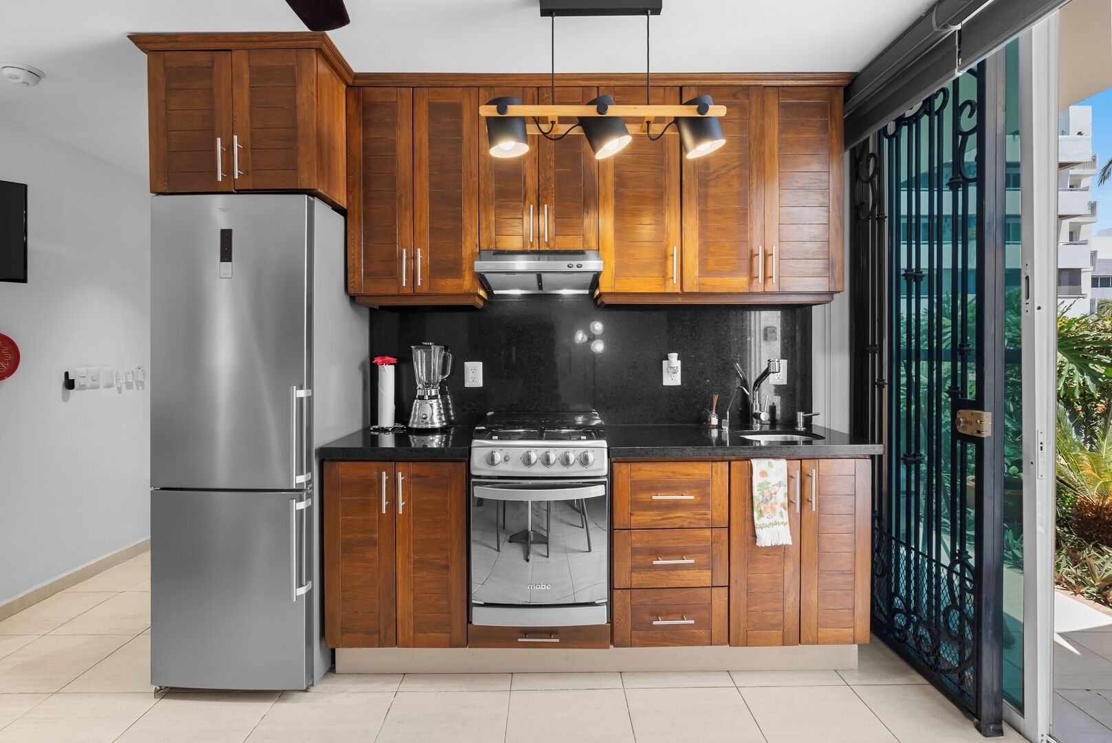 A compact kitchen with wooden cabinets, a stainless steel refrigerator, a gas stove, and a black countertop.