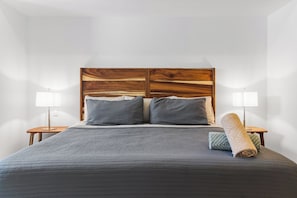 A bed with a wooden headboard, two bedside tables with lamps, and a rolled-up towel on the bed.