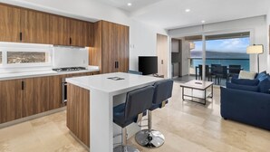A modern kitchen with wooden cabinets, a central island, and a dining area with a sofa and table. - Luxurious oceanfront condo (Puerto Vallarta)